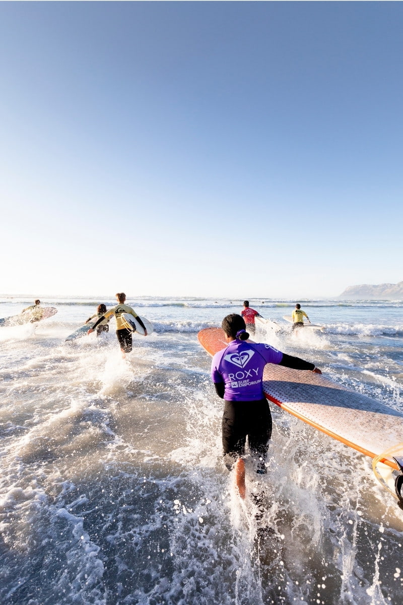 Young surfers sprint into the sea on Muizenberg beach, False Bay, South Africa