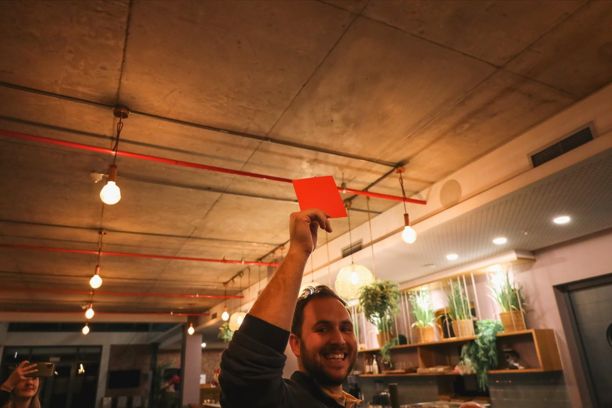 A man raising a red card during a Cape Town wine club tasting session.
