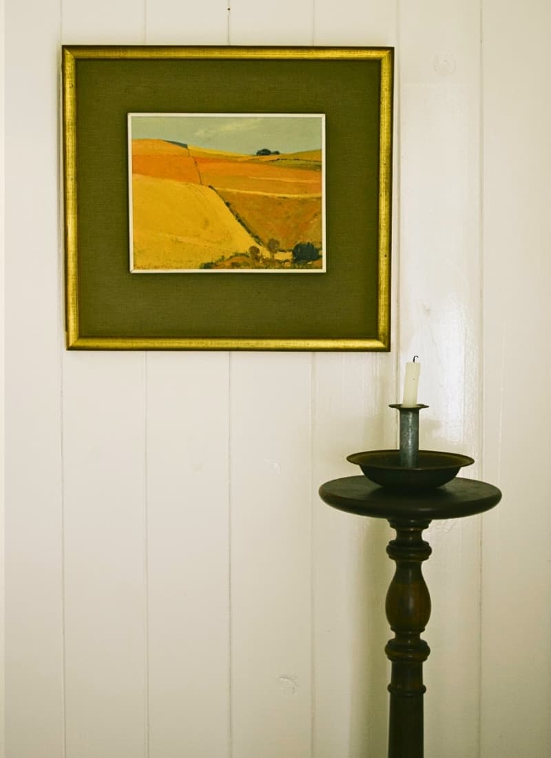 Painting and antique standing candle against a wood-panelled wall at this Piketberg farm stay