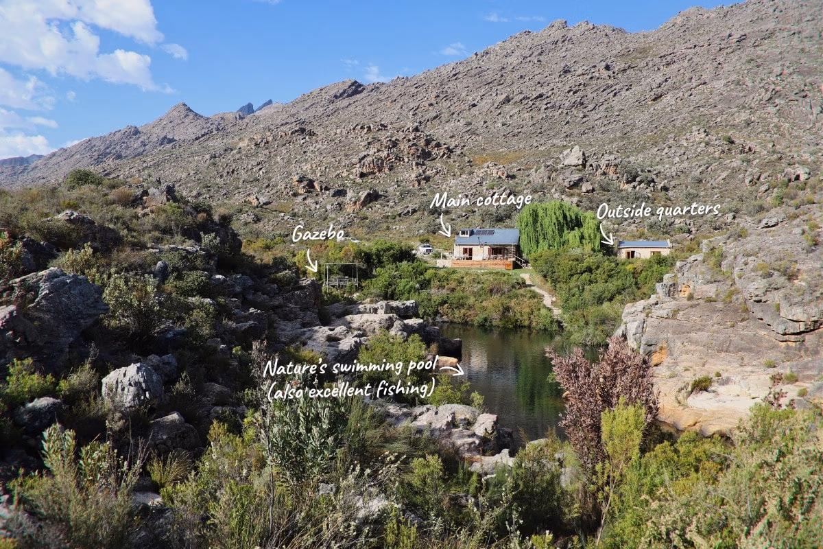 Aerial view of GlenDonald Cottage with its buildings, natural swimming pool and surrounding mountains.