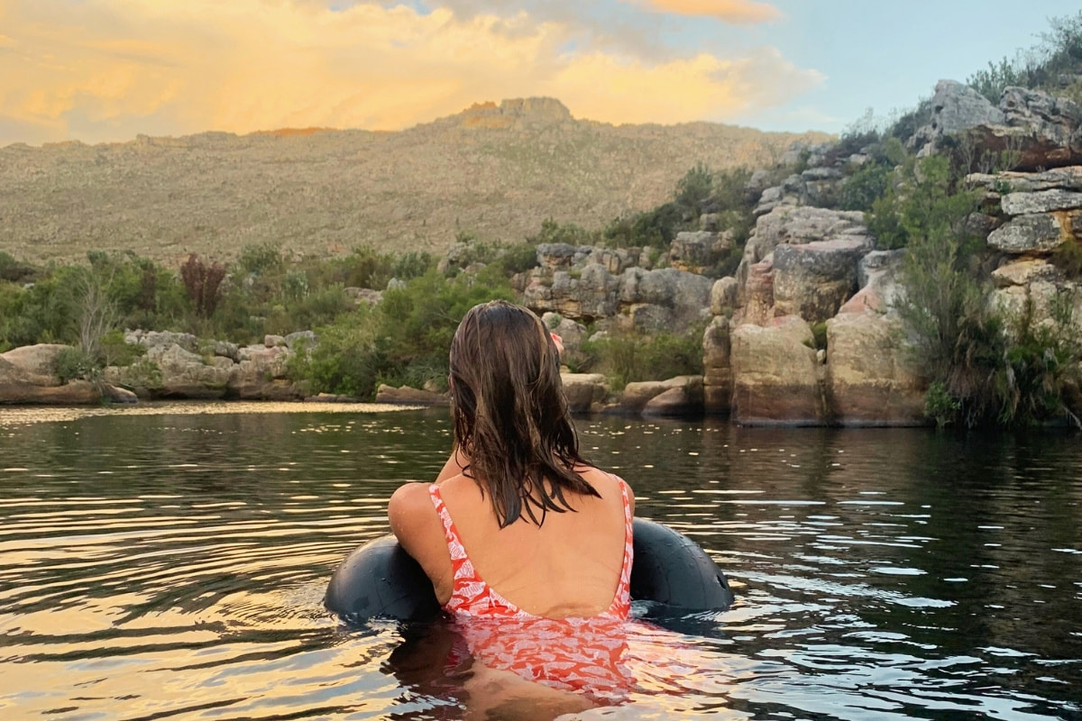 A woman floating on a tube in a river at sunset, facing the Winterhoek mountains