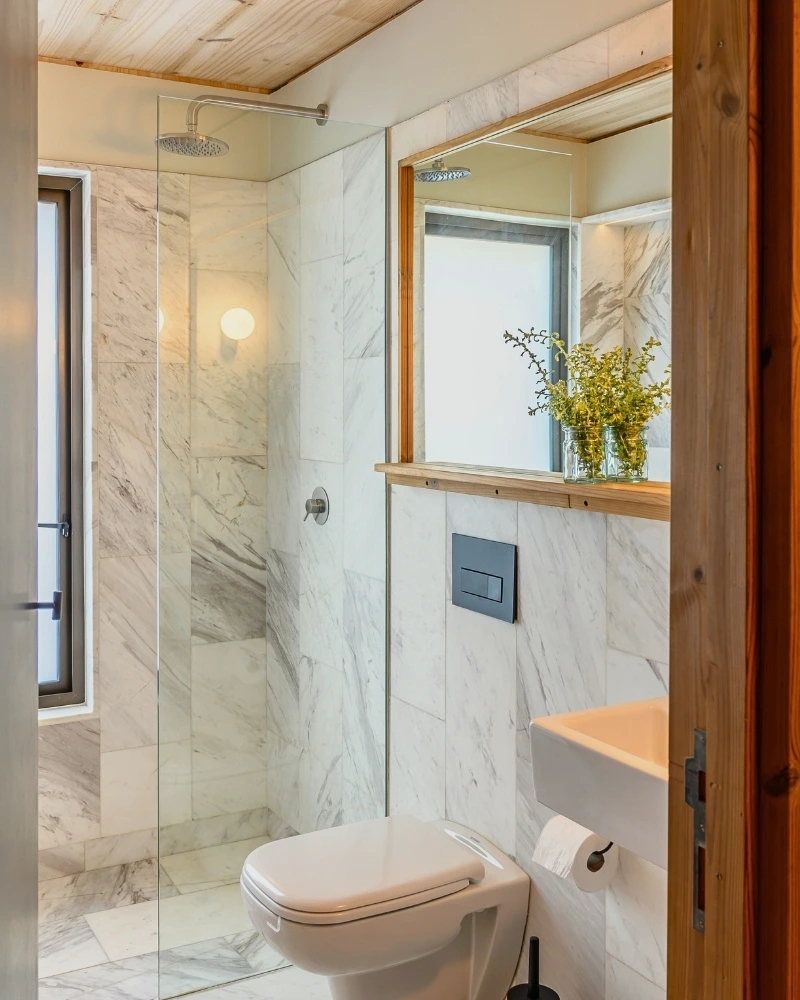 Marble-clad shower at Licorne Studio in Muizenberg, with the toilet sharing the same room behind a single glass partition.