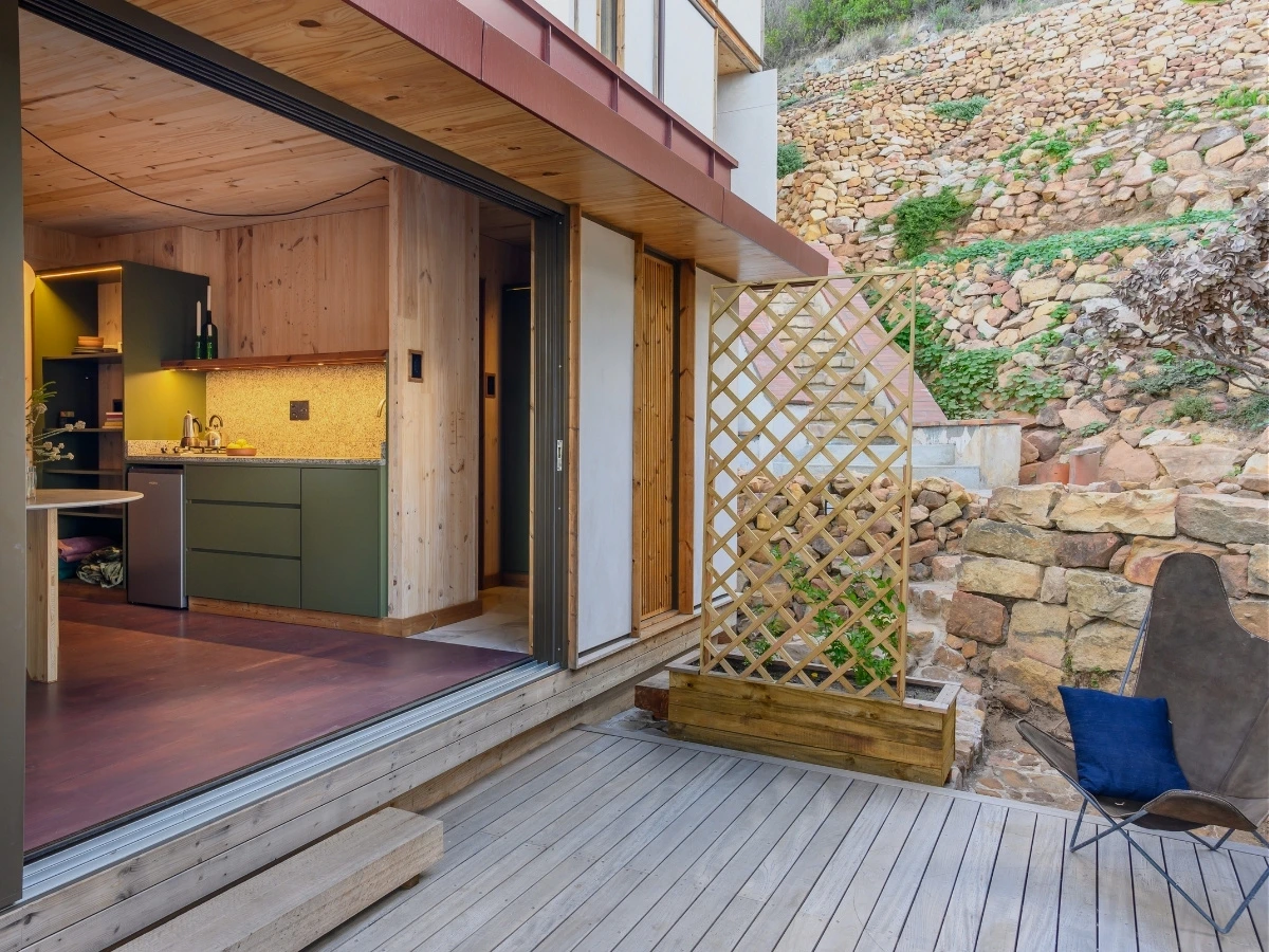 Wooden deck at Licorne Studio and a step raised above the ground so small fauna can't enter the dwelling, with stone gabion walls behind built from rock unearthed during the build.