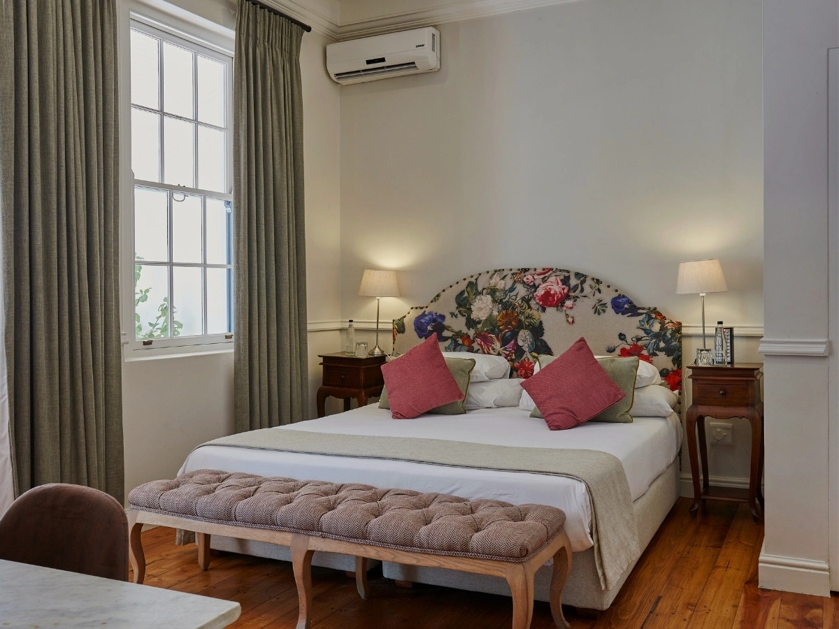 Superior pool room in the 1888 heritage wing of Chapter House Franschhoek, has a headboard in a floral pattern, beautiful sash windows.
