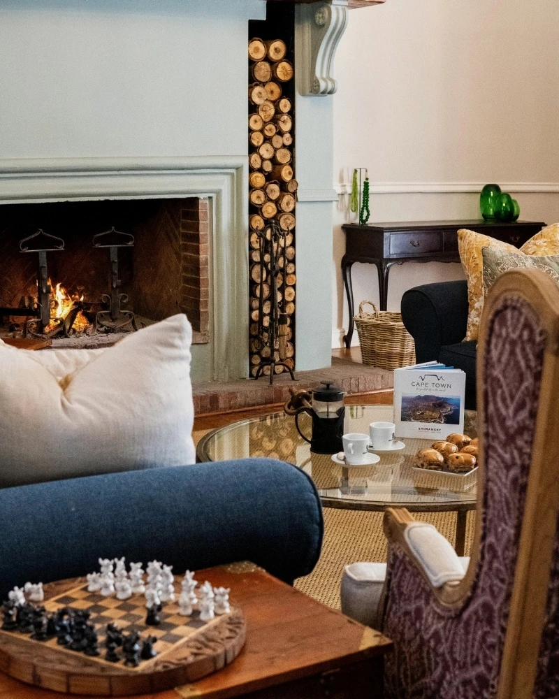 The double-volume lounge in Chapter House's 1888 heritage wing with a lit fireplace and chess board, Franschhoek