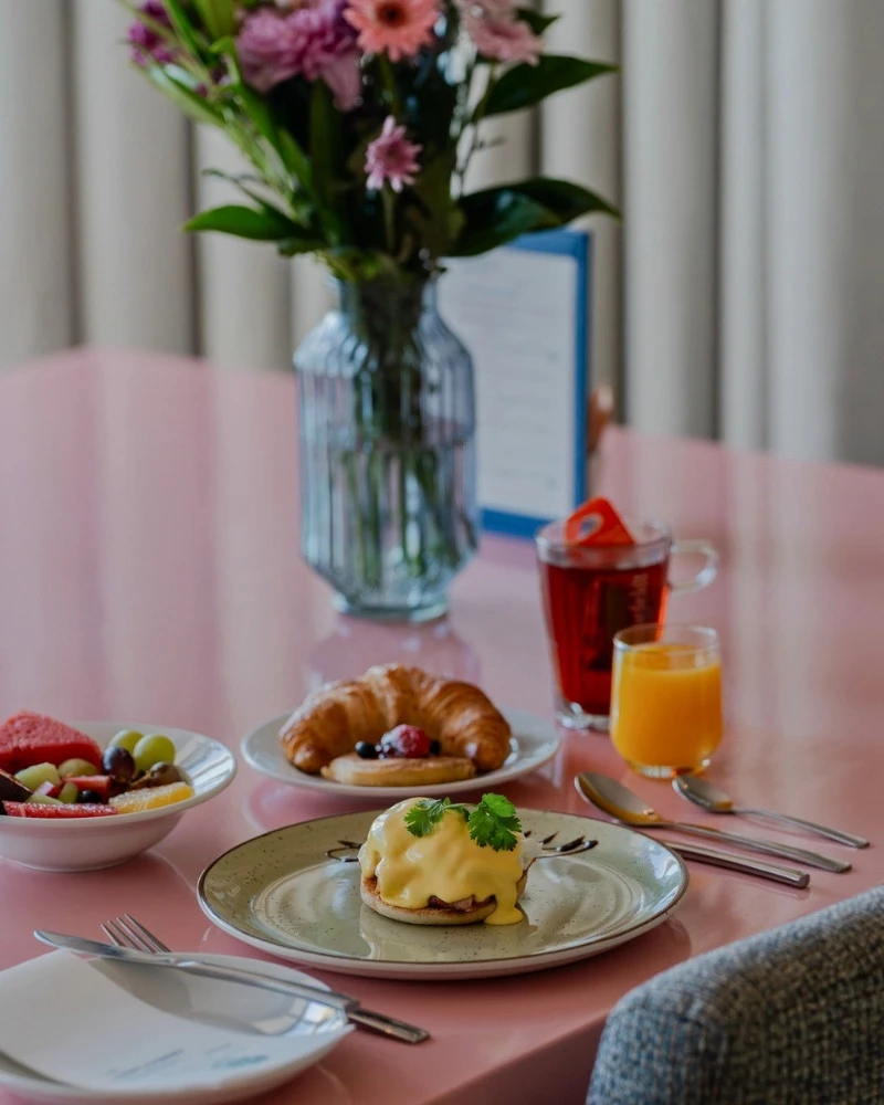 Breakfast of croissant and eggs benedict on a pink table at One Marine Drive Boutique Hotel