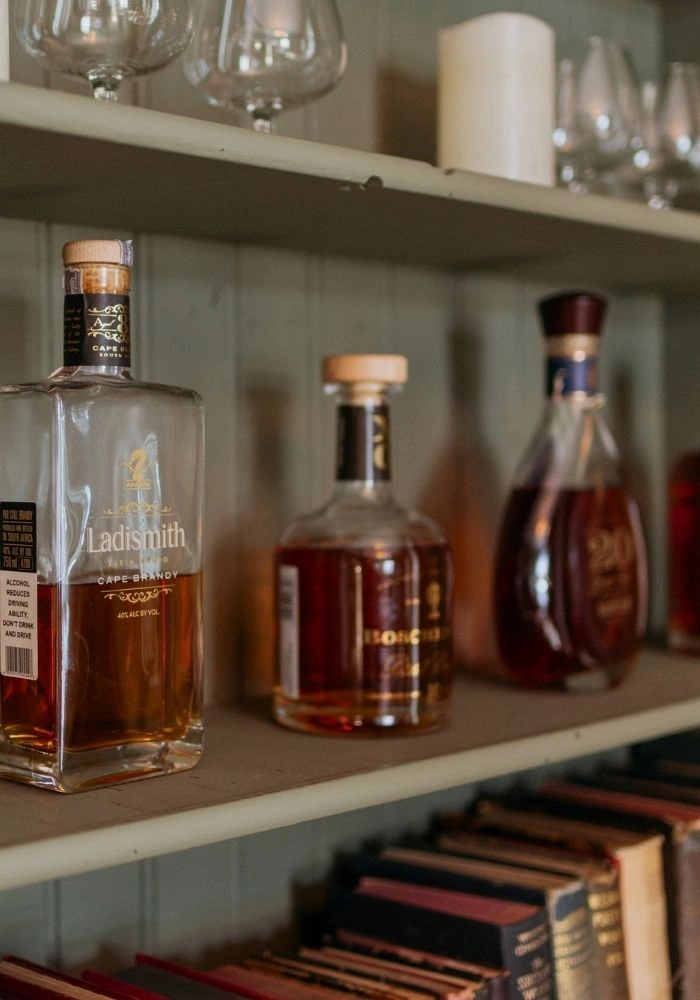 A row of whisky bottles on a green shelf with books.