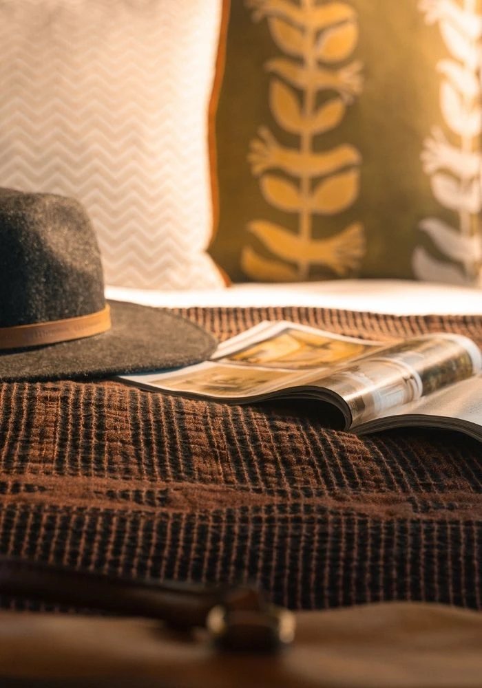 African jacquard bedspread with a hat and magazine laid on the bed in a Veldt Haus cottage at De Wildeveldt
