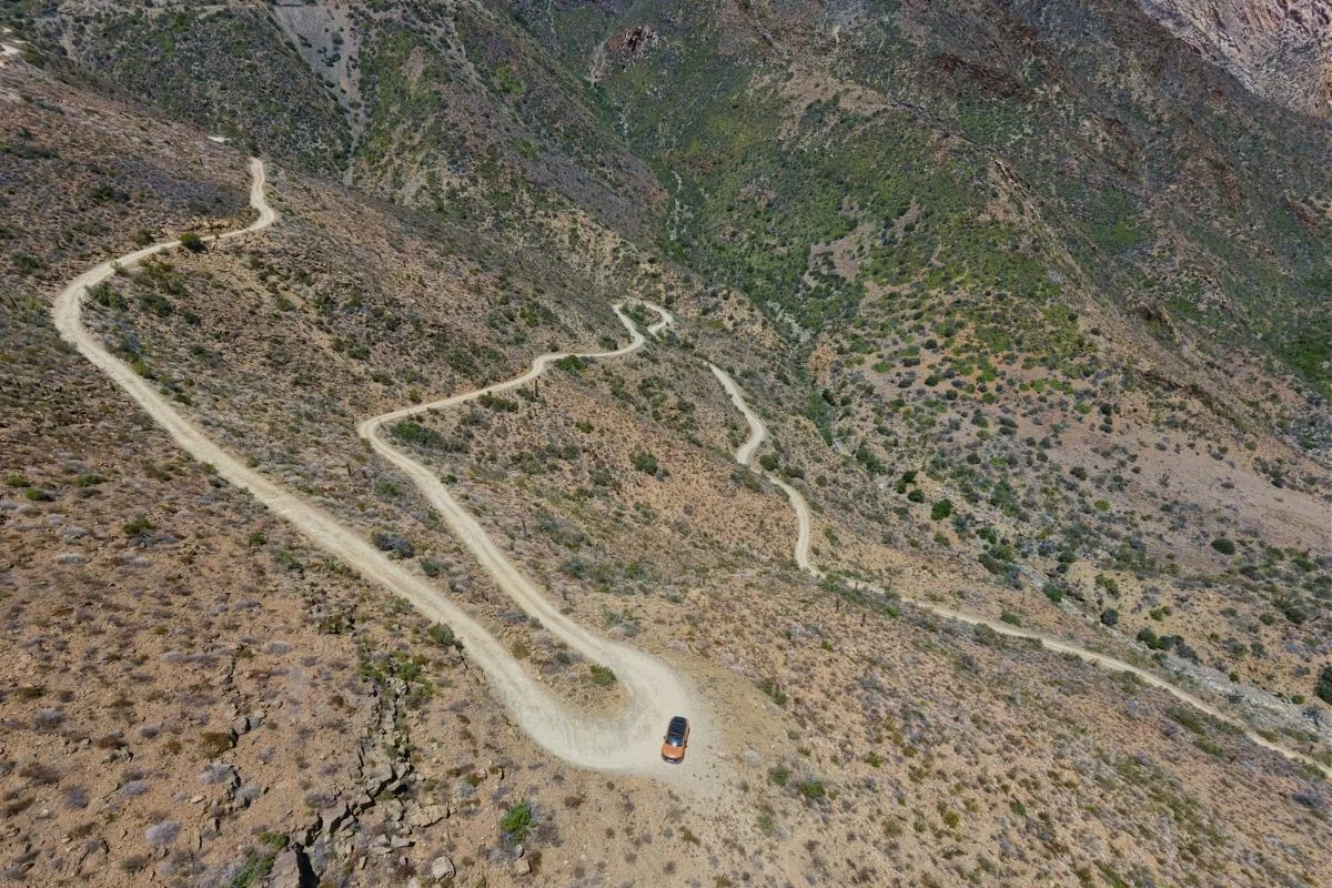 Aerial view of the winding gravel road into Gamkaskloof, with a small orange car on one of the bends.