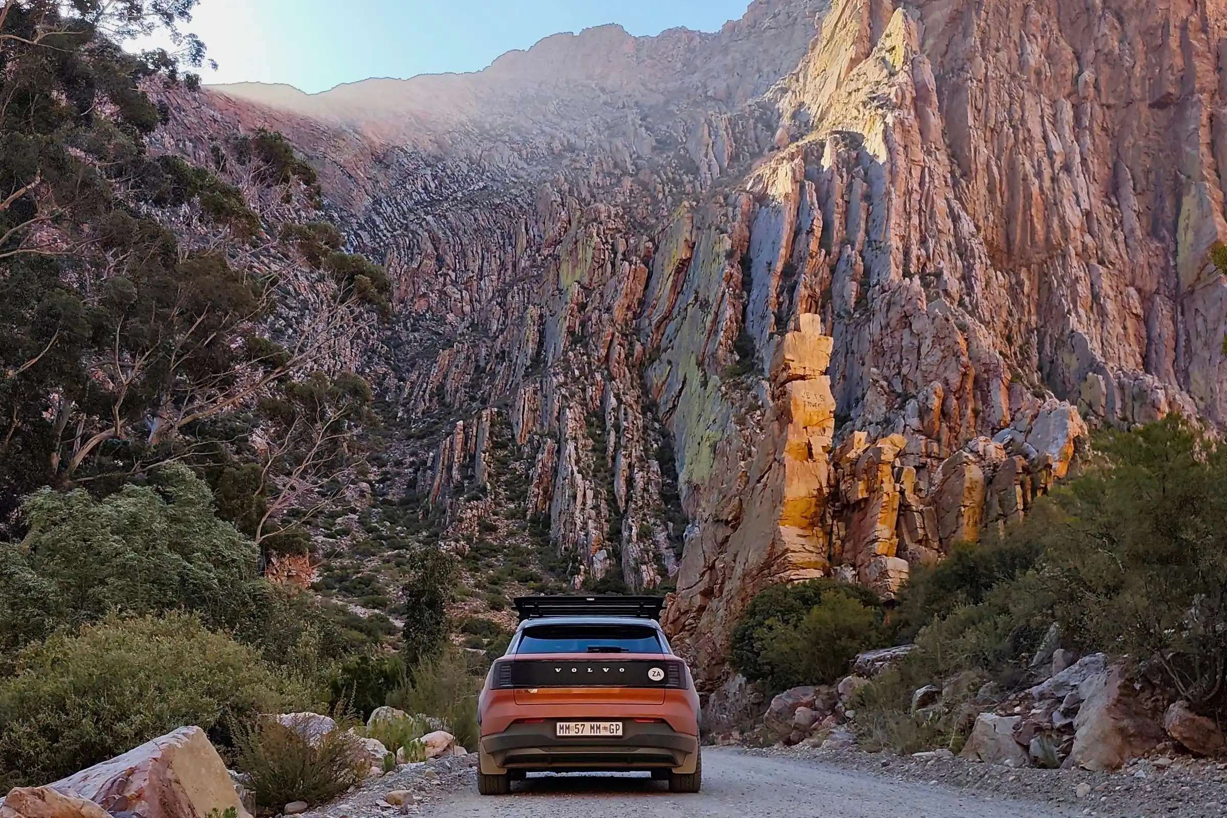 Volvo EX30 driving down a curving gravel section of the Swartberg Pass between steep mountain slopes