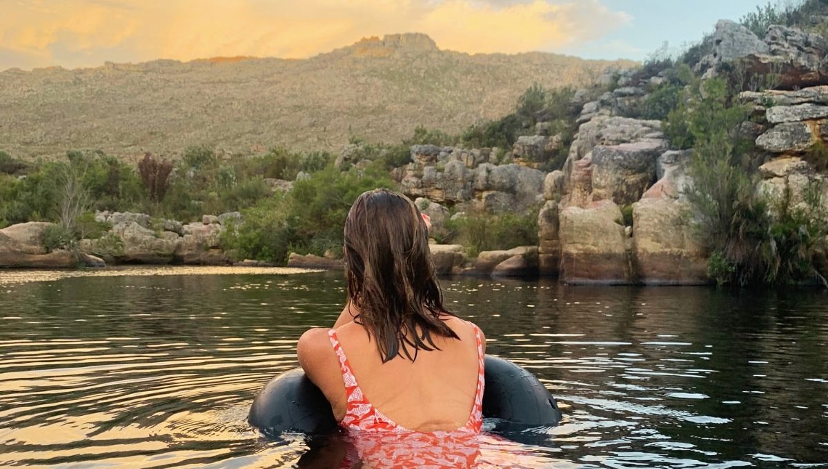 A woman floating on a tube in a river at sunset, facing the Winterhoek mountains
